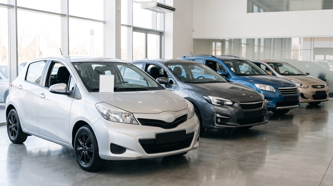 Aydınlık bir galeride sıralanmış ikinci el otomobiller; öndeki aracın torpidosunda boş bir bilgi kartı duruyor